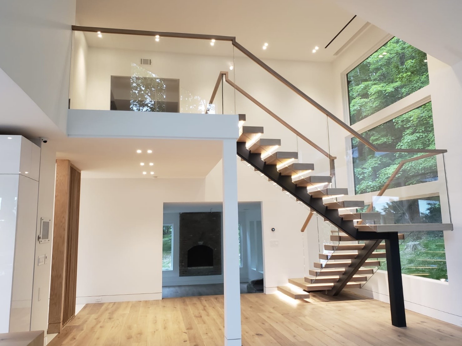 Bright and airy modern home interior featuring a floating wooden staircase with glass railing and large windows.