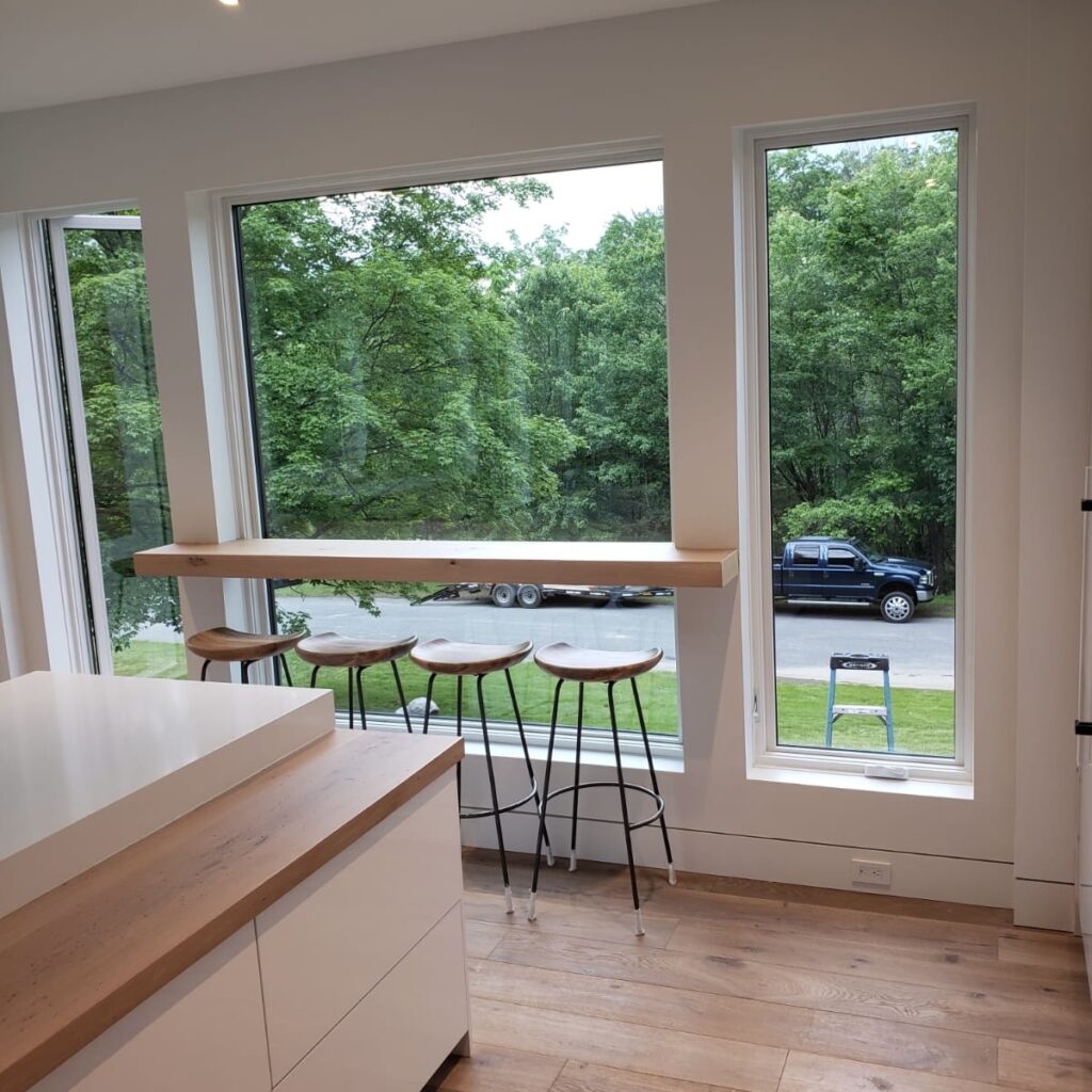 Contemporary kitchen nook with a wooden bar top and stools overlooking large windows with a view of greenery.