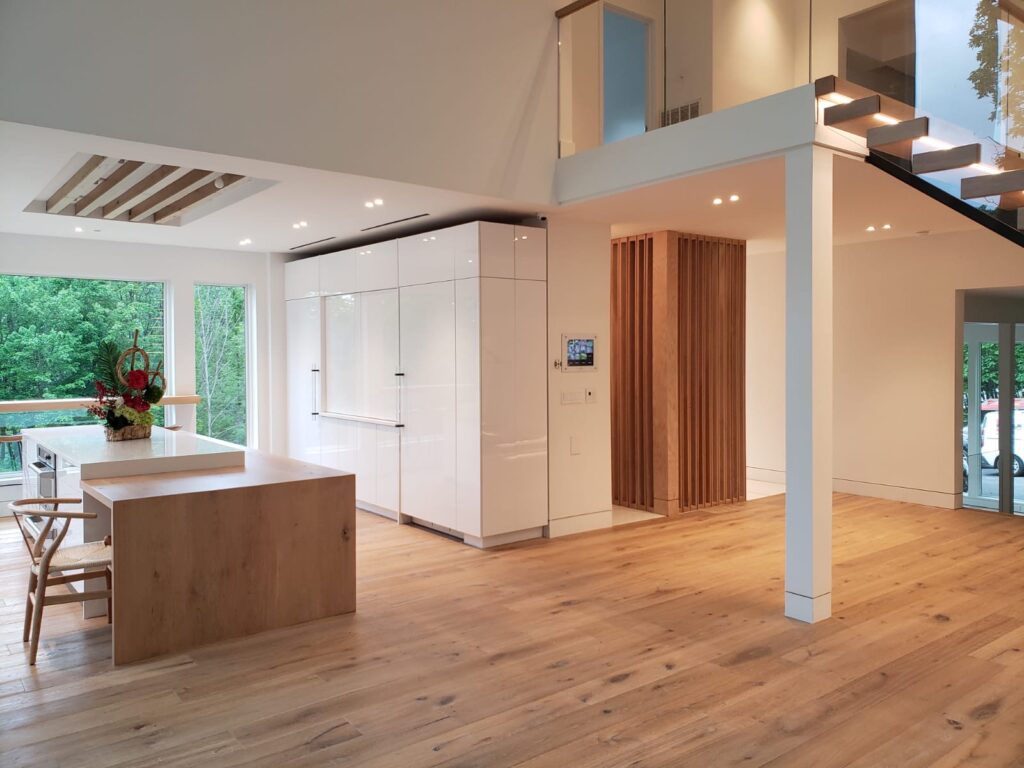 Spacious kitchen interior with wooden flooring, featuring a large island and sleek white cabinetry.