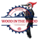 Logo of Wood In the Blood, showcasing a detailed woodpecker perched on a red and blue circular saw blade, symbolizing expert custom millwork.